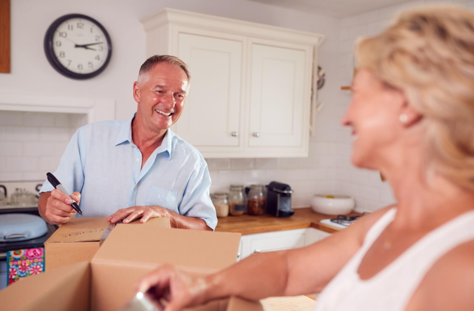 A senior couple packing kitchen items away into boxes and labelling them to sort items to keep from items to donate easier