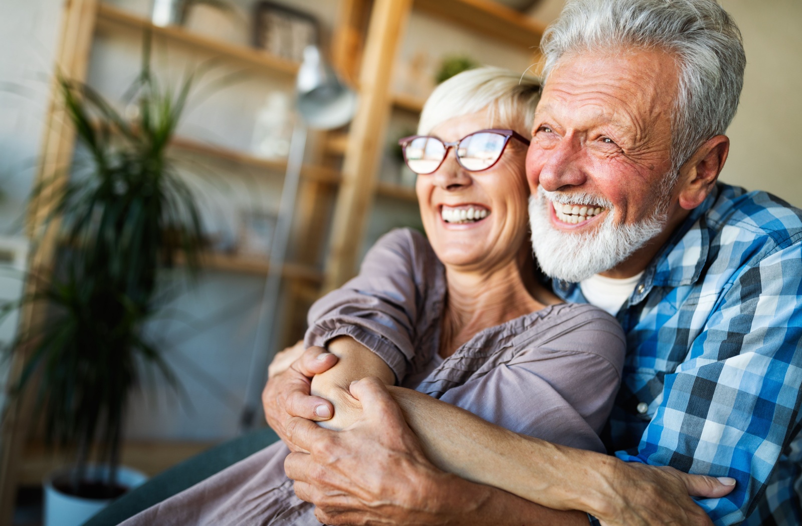A senior couple shares a warm embrace, their faces glowing with big, happy smiles.