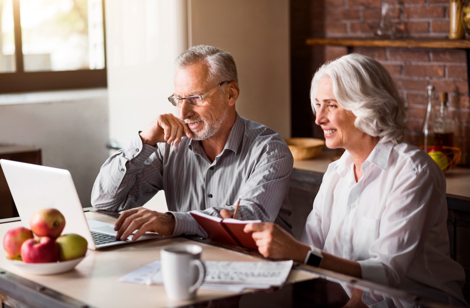 An older couple sitting in their kitchen with a laptop and notebook researching senior living communities.