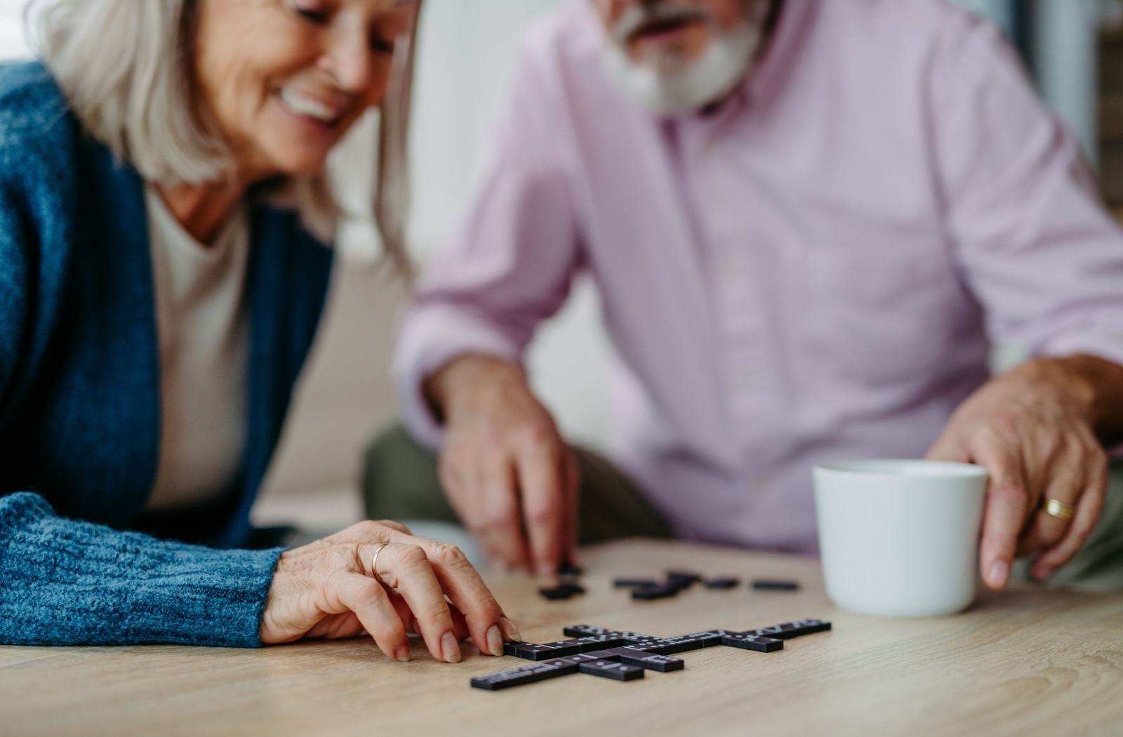 Two seniors with dementia play a game of dominoes together on a polished wood coffee table