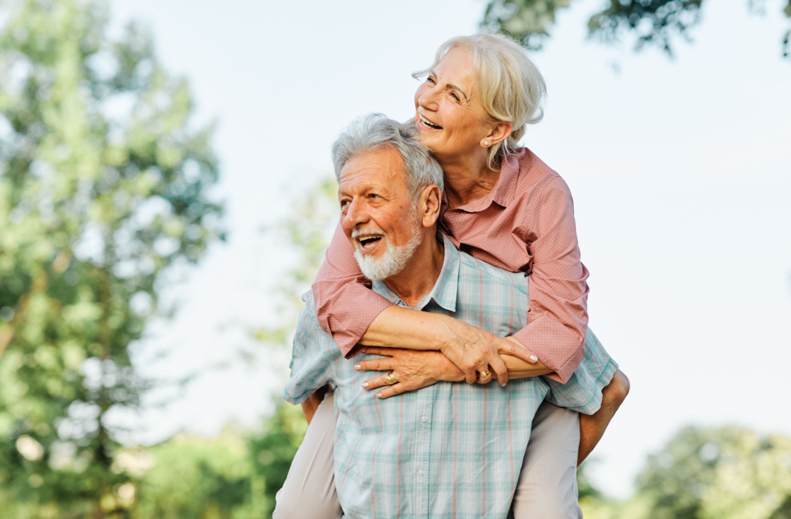 A senior gives their partner a piggyback ride while enjoying a beautiful spring day outside