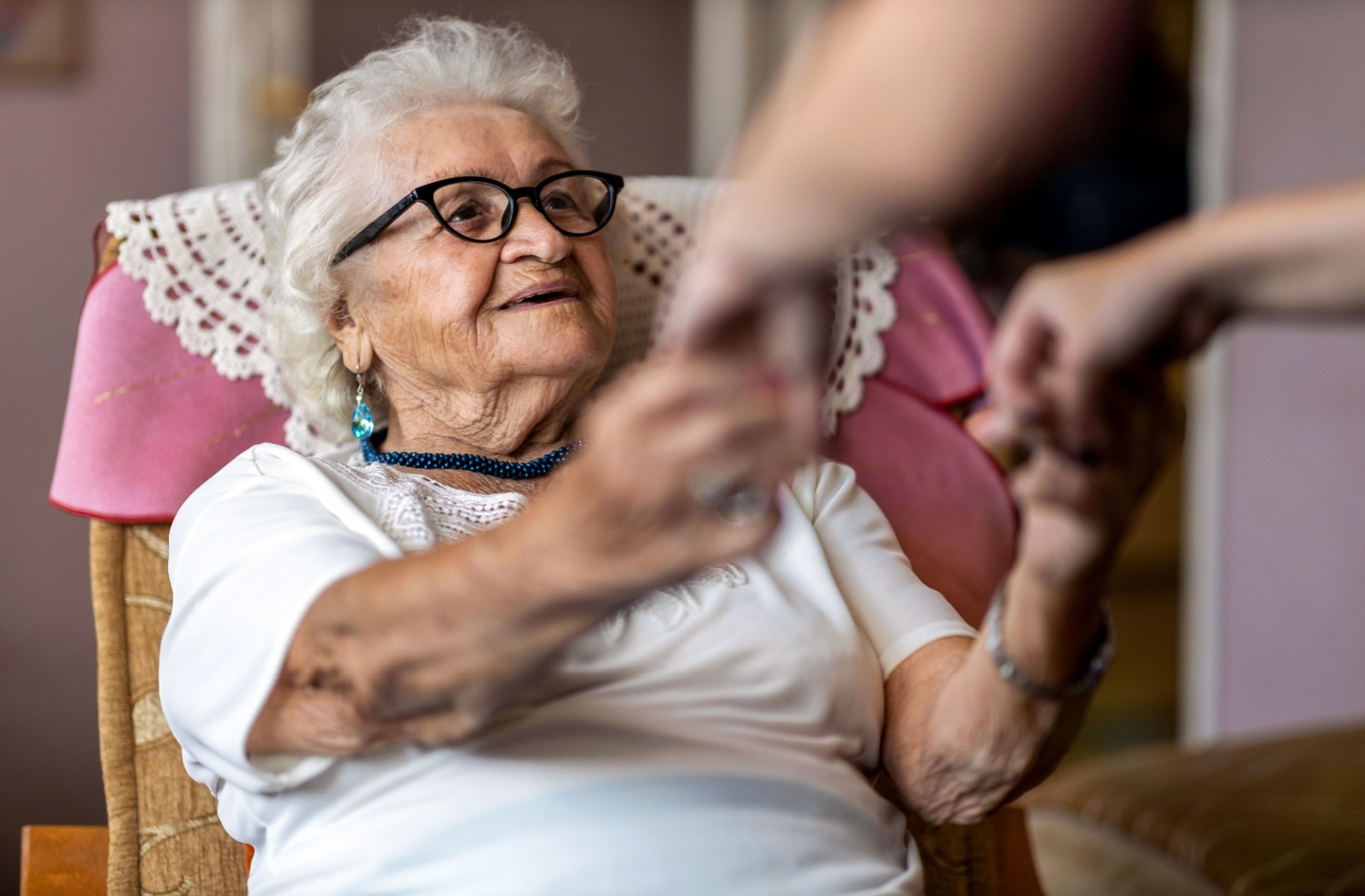 A senior living with dementia holds hands with their loved one while sitting in a chair.