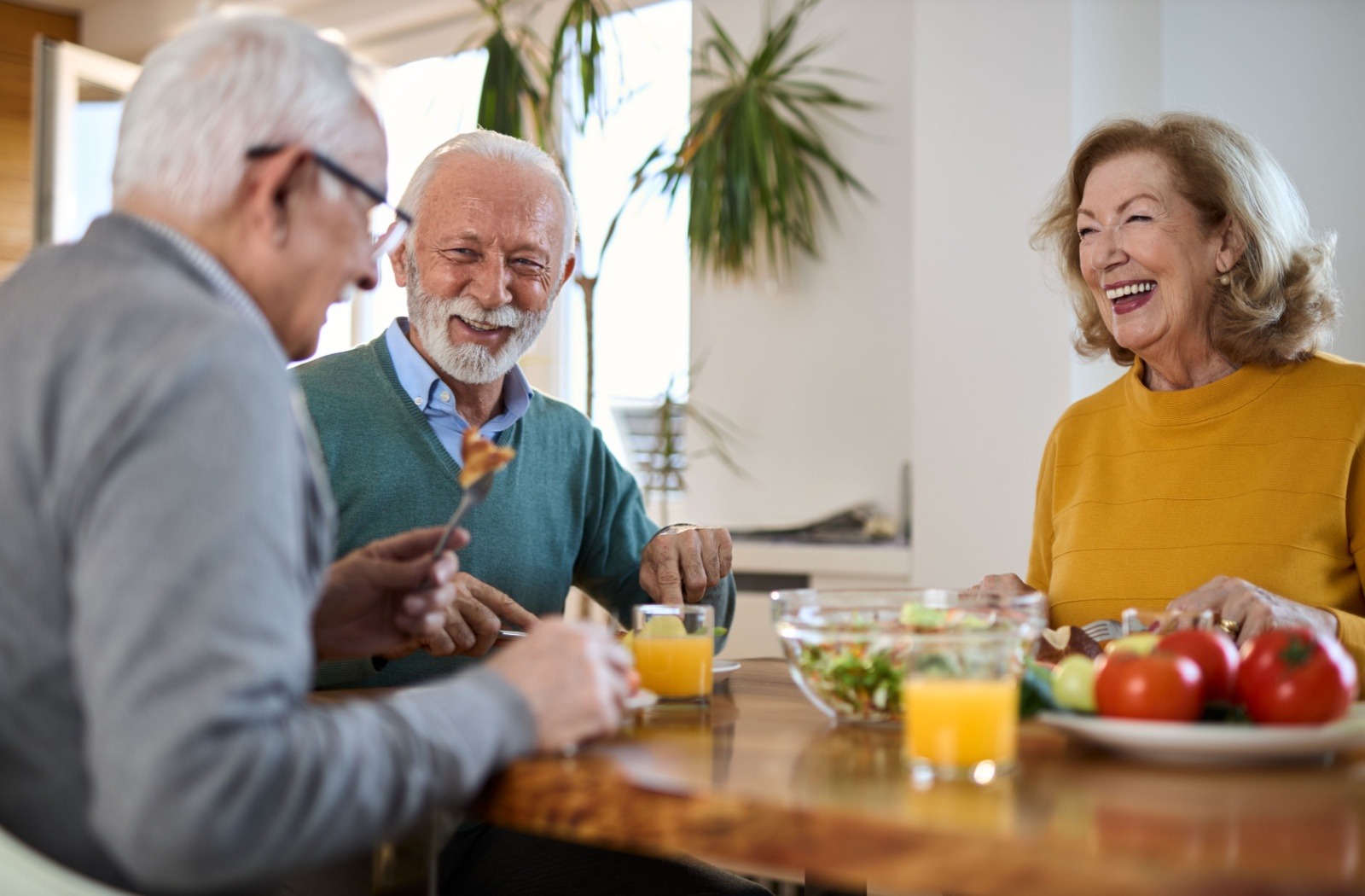 A group of senior friends smile as they enjoy breakfast together at an independent living community.
