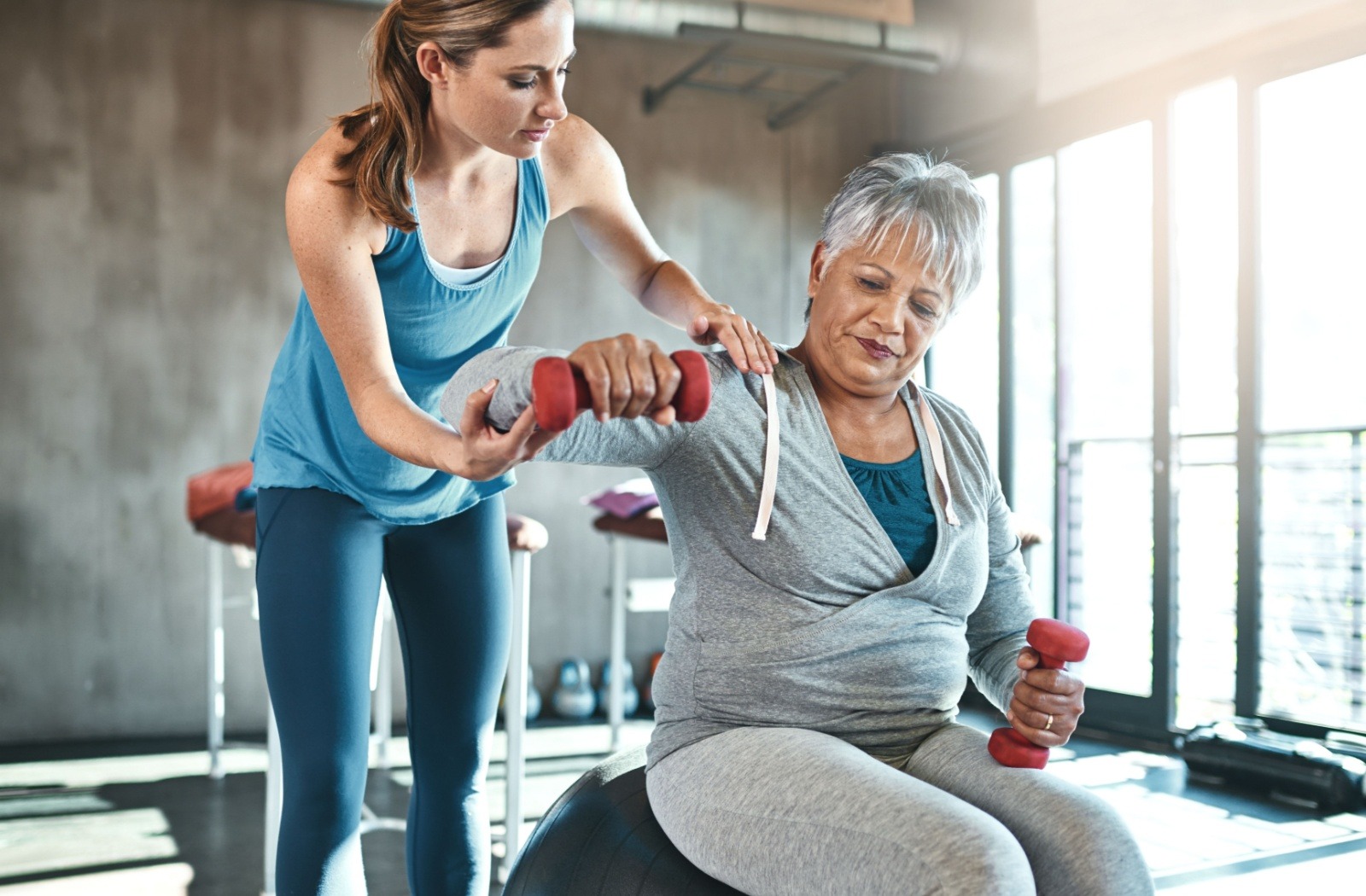 A senior works out in a gym at a senior living community, under the guidance of a personal trainer.
