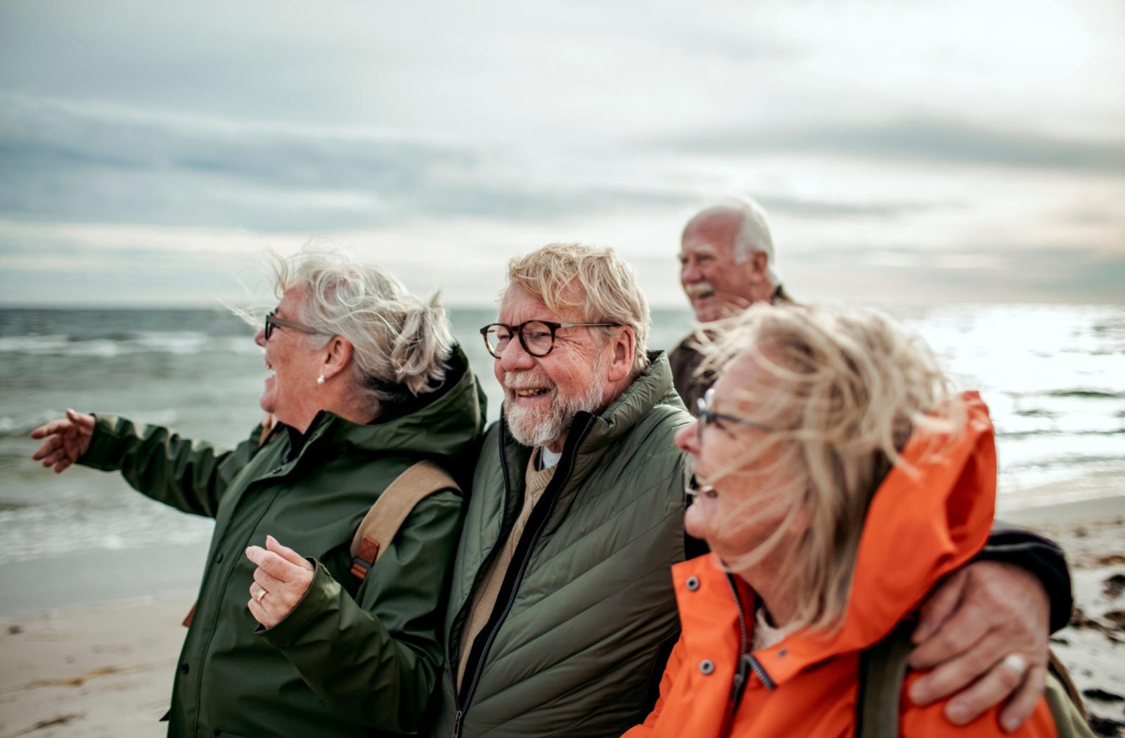 A group of 4 active seniors enjoy a walk on a beach on a brisk fall day.