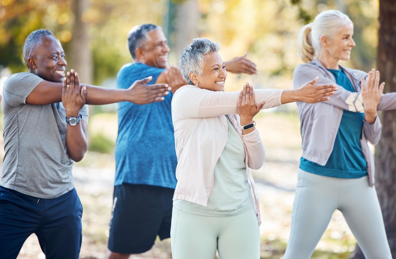 A group of senior friends stretch together during an outdoor workout class at a senior living community.